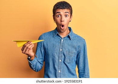 Young African Amercian Man Holding Paper Airplane Scared And Amazed With Open Mouth For Surprise, Disbelief Face 