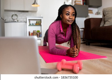 Young African America Woman At Home Doing Exercise In Front Of Open Laptop, Repeating Instructions By Professional Online Fitness Trainer.