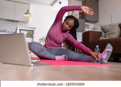 Young African America Woman At Home Doing Exercise In Front Of Open Laptop, Repeating Instructions By Professional Online Fitness Trainer.