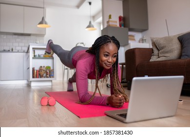 Young African America Woman At Home Doing Exercise In Front Of Open Laptop, Repeating Instructions By Professional Online Fitness Trainer.