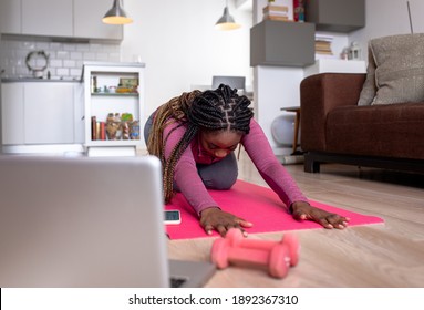 Young African America Woman At Home Doing Exercise In Front Of Open Laptop, Repeating Instructions By Professional Online Fitness Trainer.