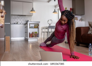 Young African America Woman At Home Doing Exercise In Front Of Open Laptop, Repeating Instructions By Professional Online Fitness Trainer.