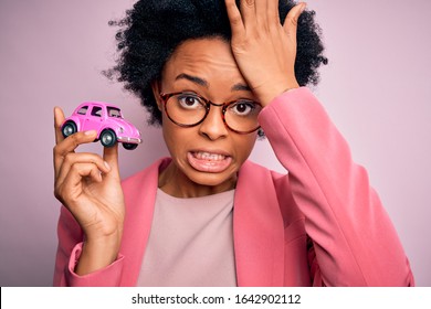 Young African American Afro Woman With Curly Hair Holding Car Toy Over Pink Background Stressed With Hand On Head, Shocked With Shame And Surprise Face, Angry And Frustrated. Fear And Upset