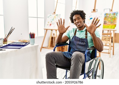 Young african american artist man sitting wheelchair at art studio showing   pointing up and fingers number ten while smiling confident   happy  