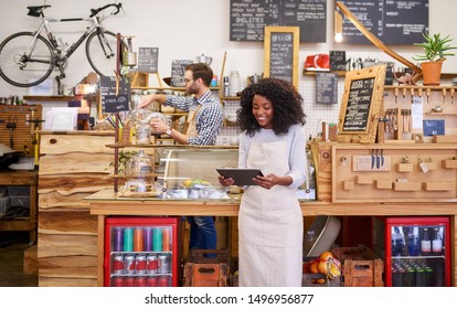 Young African American barista smiling while standing in front of the counter of a trendy cafe using a digital tablet - Powered by Shutterstock