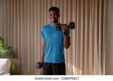 Young African American Black Male Doing Bicep Curls Using Dumbells And Doing An Intense Weight Training, Working Out At Home Gym.