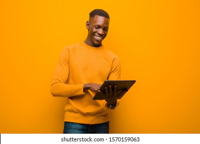 Young African American Black Man Against Orange Wall With A Smart Tablet