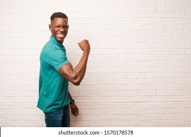 young african american black man feeling happy, satisfied and powerful, flexing fit and muscular biceps, looking strong after the gym against brick wall