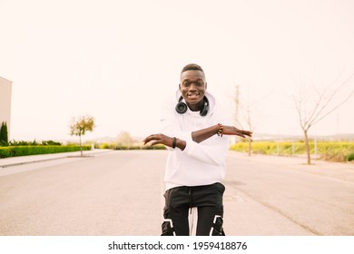 Young African American Black Man With Afro Hair Dancing In The Middle Of The Street Wearing A White Sweatshirt, Black Pants And Wireless Headphones. Happy And Joy Attitude