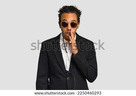 Young African American bodyguard man isolated is saying a secret hot braking news and looking aside