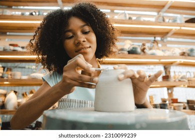 Young African American boy and girl wearing apron preparing pots and sculptures using mud and and clay and painting them in a workshop studio while decorating them using brushes - Powered by Shutterstock