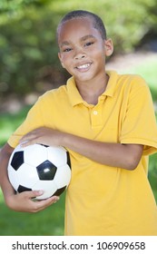 A Young African American Boy Outside Playing Soccer Or Football On The Grass In A Park Or Garden