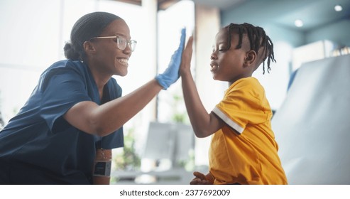 Young African American Boy Sitting In The Chair In Bright Hospital And Getting His Flu Vaccine. Female Black Nurse Is Finished Performing Injection. Professional Woman High-Fives A Kid For Being Brave - Powered by Shutterstock