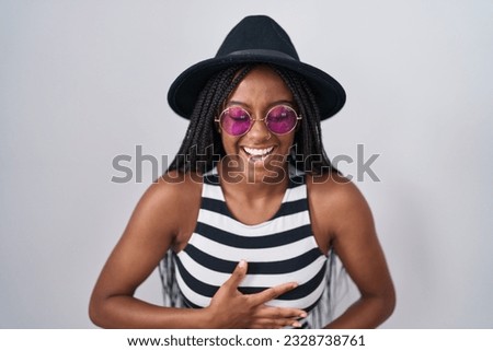 Young african american with braids wearing hat and sunglasses smiling and laughing hard out loud because funny crazy joke with hands on body. 
