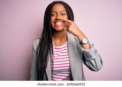 Young african american business woman standing over pink isolated background Pointing with hand finger to face and nose, smiling cheerful. Beauty concept