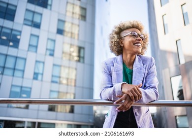 Young African American business woman in trendy outfit and eyeglasses standing on corporate urban district. Inspired creative female professional in the city - Shutterstock ID 2106161693