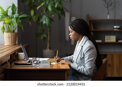 Young African American Business Woman, Trainee Or Ceo Work Online With Laptop Make Notes For Presentation Sitting At Office Desk. Focused Female Professional Preparing Report Paperwork At Workplace