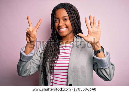 Young african american business woman standing over pink isolated background showing and pointing up with fingers number seven while smiling confident and happy.