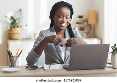 Young african american businesswoman drinking coffee while working on laptop in modern office
