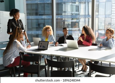 Young African American businesswoman lead meeting with multiethnic colleagues, communicate interact in office. Female ethnic coach or boss present at workplace, brainstorm with diverse businesspeople.