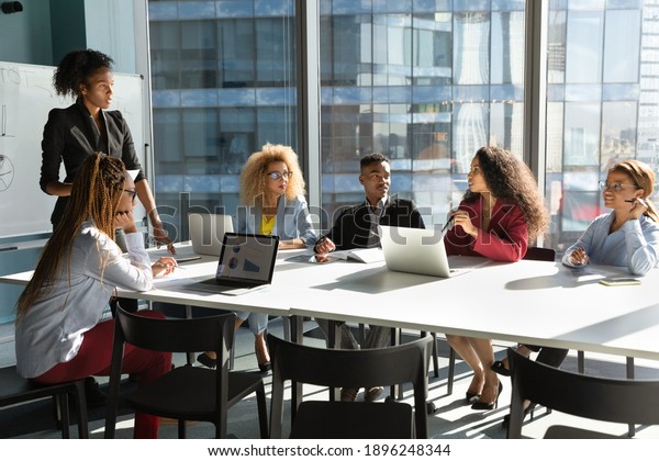 Young African American businesswoman lead\
meeting with multiethnic colleagues, communicate interact in\
office. Female ethnic coach or boss present at workplace,\
brainstorm with diverse\
businesspeople.