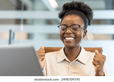 Young African American businesswoman looking excited and happy while working on laptop in office. Concept of success and achievement in business environment. Modern workplace setting. - Powered by Shutterstock