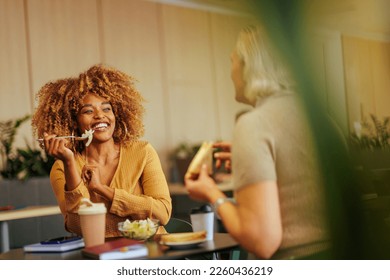 A young African American businesswoman is on a lunch break in the office canteen with her coworker enjoying the conversation. - Powered by Shutterstock