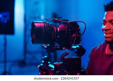 Young African American cameraman working with professional camera and shooting process in studio
