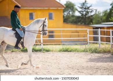 Young African American in casual outfit riding white horse on sandy ground on ranch - Powered by Shutterstock