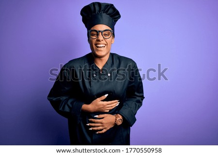 Young african american chef girl wearing cooker uniform and hat over purple background smiling and laughing hard out loud because funny crazy joke with hands on body.