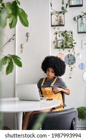 Young African American College Student Hipster Woman With Afro Hair Sitting At Table In Cafe Indoor Using Laptop Watching Learning Virtual Online Digital Webinar.