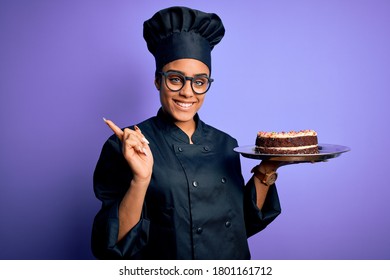 Young African American Cooker Girl Wearing Uniform And Hat Holding Tray With Cake Very Happy Pointing With Hand And Finger To The Side