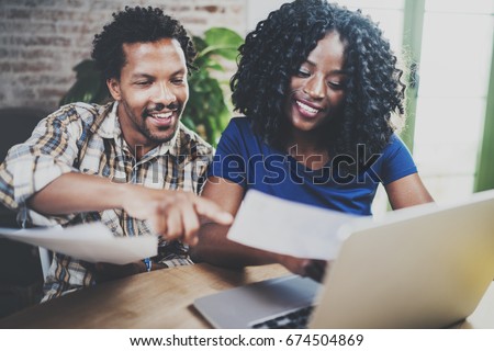 Young African american couple checking bills together at the wooden table.Young black man and his girlfriend using laptop while working at home. Horizontal,blurred background.Cropped