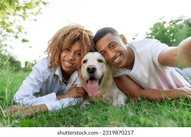 young african american couple with dog lie in park on green grass and take selfie, curly woman and young man take photo together with golden retriever, young happy family with pet in nature - Powered by Shutterstock