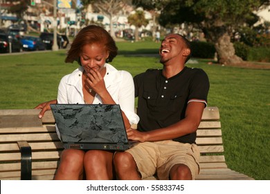 A Young African American Couple Enjoy Using A Laptop Computer Outside