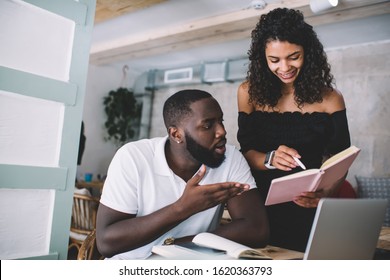 Young African American Couple Of Freelancers Working In Cafe And Cheerful Woman Showing Notes In Diary To Surprised Male Colleague