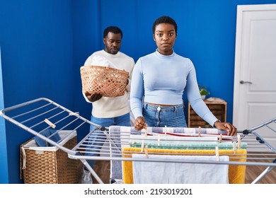 Young African American Couple Hanging Clothes At Clothesline Thinking Attitude And Sober Expression Looking Self Confident 