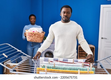 Young African American Couple Hanging Clothes At Clothesline Thinking Attitude And Sober Expression Looking Self Confident 