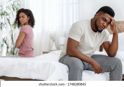Young african american couple having relationships crisis, upset man and woman sitting separated on bed, empty space between them