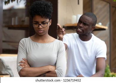 Young African American couple in love quarrelling sitting together on couch, angry man blaming upset frustrated woman with hands crossed, girlfriend offended by mad boyfriend, break up concept