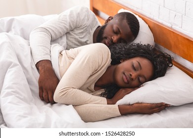 Young african american couple napping together in bed, husband cuddling his wife from back.