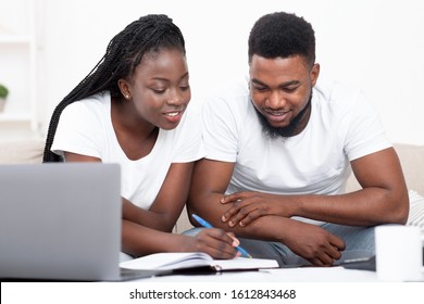 Young African American Couple Planning Budget Together At Home, Writing Notes To Notebook, Creating Checklist For Shopping Or Guest List For Wedding