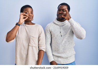 Young african american couple standing over blue background together mouth and lips shut as zip with fingers. secret and silent, taboo talking 