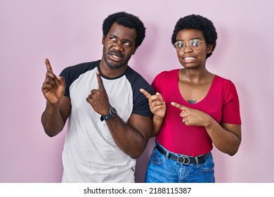 Young African American Couple Standing Over Pink Background Pointing Aside Worried And Nervous With Both Hands, Concerned And Surprised Expression 