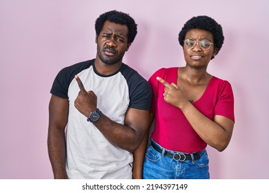 Young African American Couple Standing Over Pink Background Pointing Aside Worried And Nervous With Forefinger, Concerned And Surprised Expression 