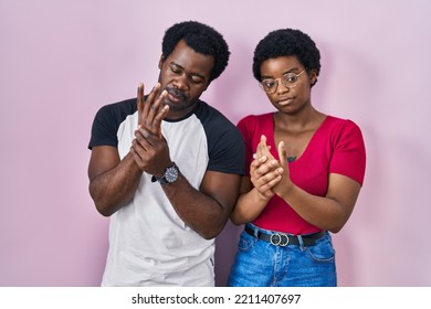 Young African American Couple Standing Over Pink Background Suffering Pain On Hands And Fingers, Arthritis Inflammation 