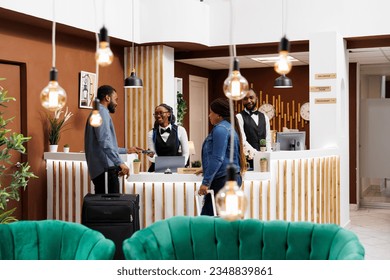 Young African American couple standing at hotel front desk with luggage, paying for room with credit card while checking out. Friendly smiling female receptionist serving tourists checking guests in - Powered by Shutterstock