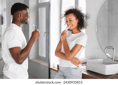 Young African American couple stands together brushing teeth indoor at bathroom, sharing daily dental care moment for wellness, smiling to each other exuding love and happiness - Powered by Shutterstock