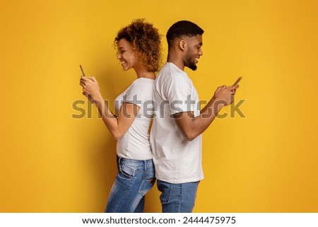 A young African American couple stands back-to-back, engrossed in their smartphones, symbolizing modern communication issues against a vibrant yellow background