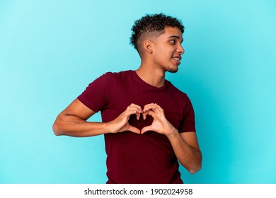 Young African American Curly Man Isolated On Blue Smiling And Showing A Heart Shape With Hands.